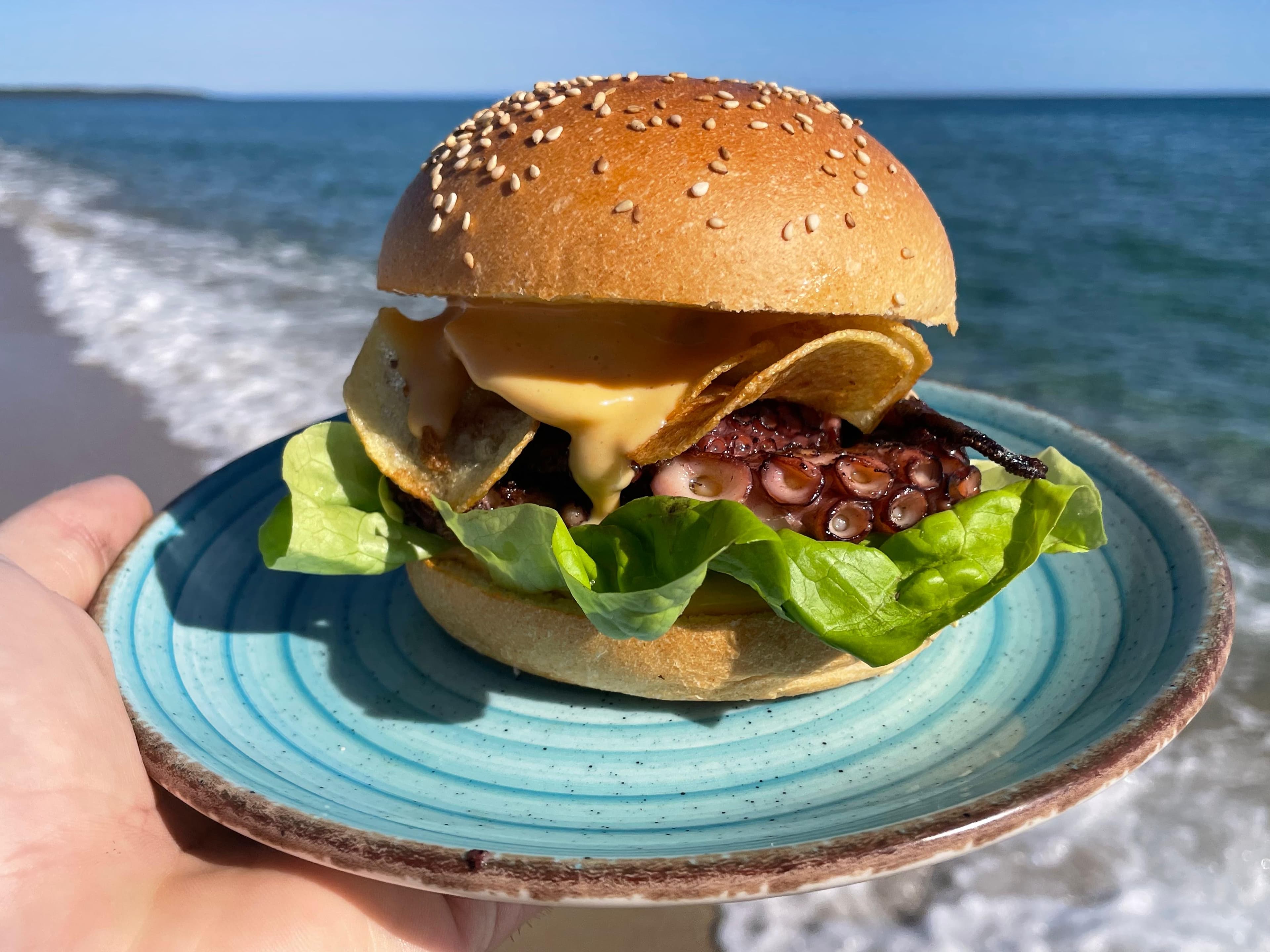 Panino con polpo servito su piatto azzurro davanti al mare